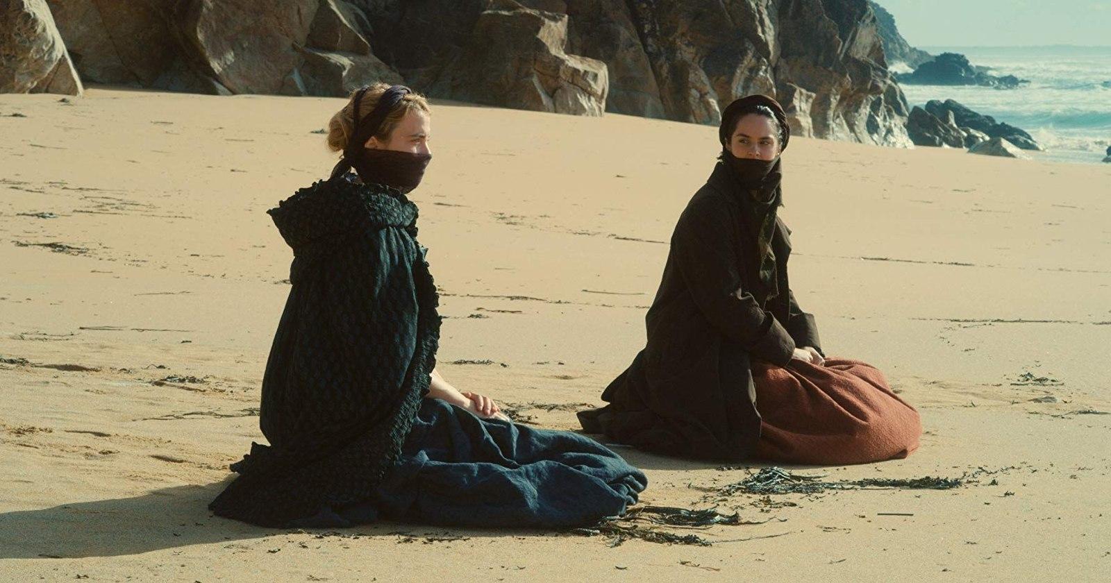 Adèle Haenel como Héloïse y Noémie Merlant como Marianne en Portrait of a Lady on Fire sentadas en la arena en la playa
