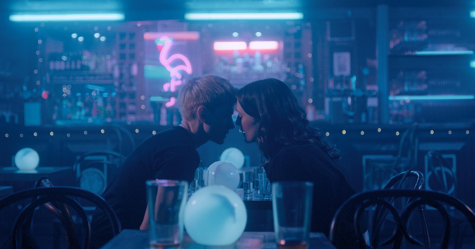 Mae y George en Feel Good, en un bar nocturno, con las caras muy cerca apunto de darse un beso.