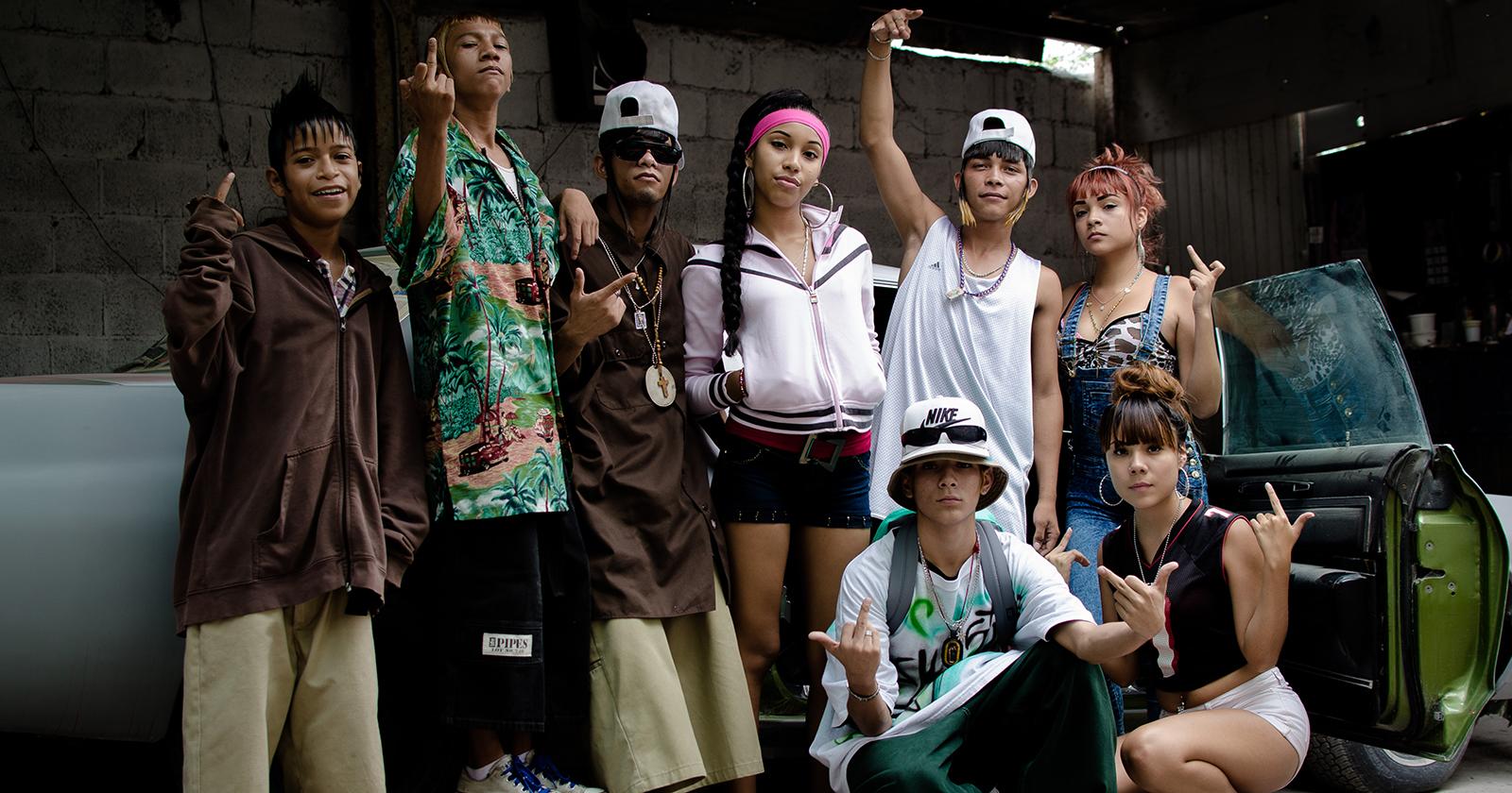 Grupo de ocho jóvenes caracterizados con la estética característica de los Kolombia. Peinados extravagantes y vestimentas coloridas y holgadas.