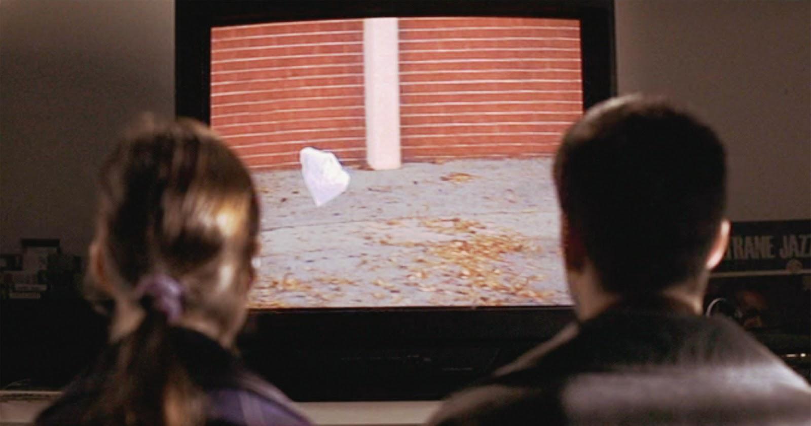 Jane (Thora Birch) y Ricky (Wes Bentley) de espaldas frente a un televisor, contemplando la famosa escena de la bolsa plástica bailando al viento.