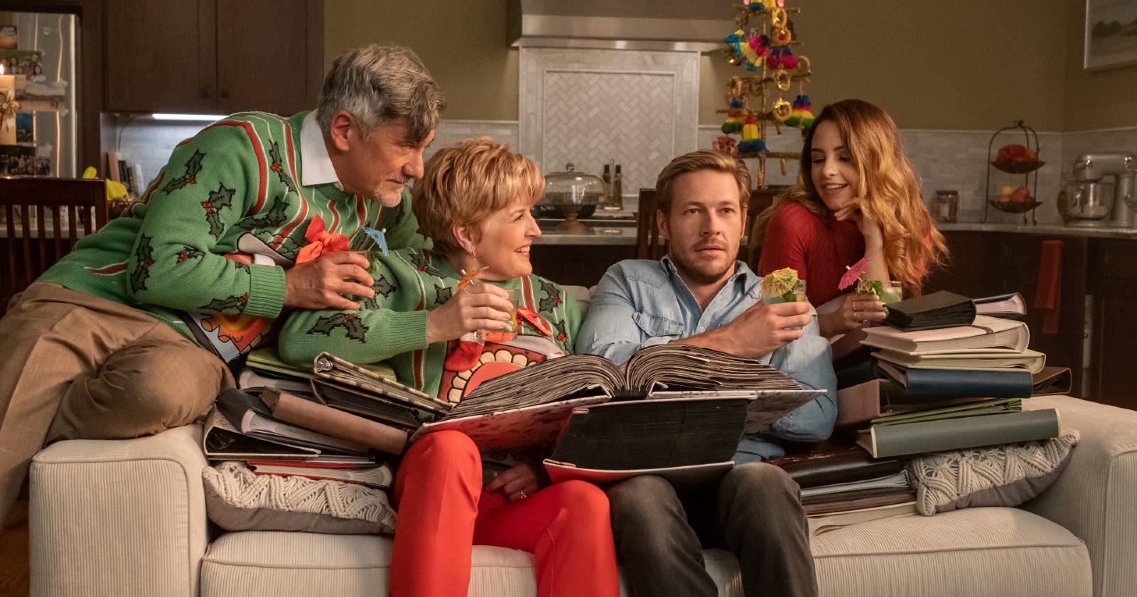 Luke Bracey como Jackson en Amor de calendario en la fiesta de navidad con la familia de su cita sentados en el sillón
