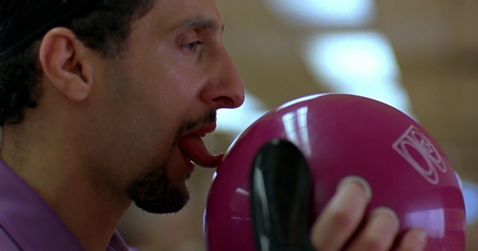John Turturro interpretando a Jesús. En la imagen pasa su lengua sobre una bola de bowling.